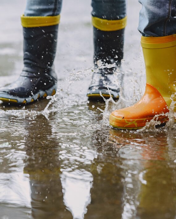 criancas_engracadas_em_botas_de_chuva_brincando_com_navio_de_papel_por_uma_poca